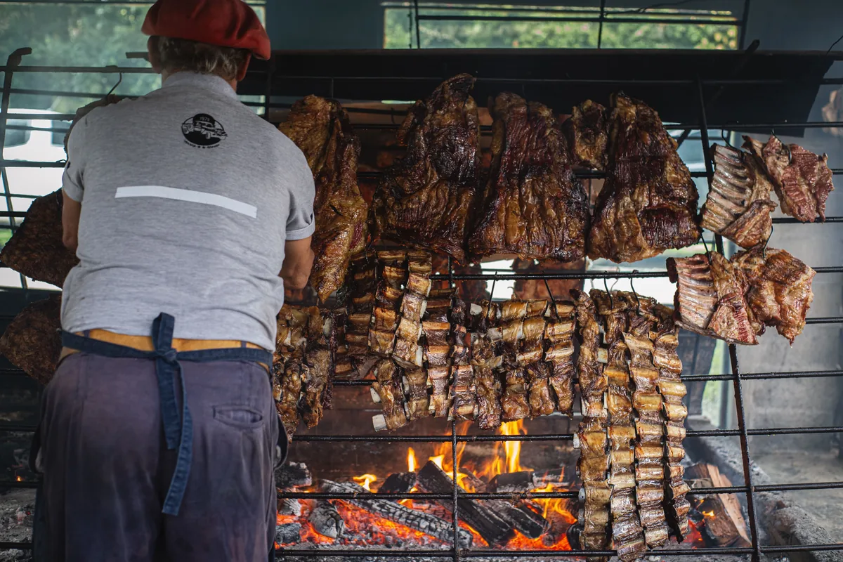 An asador tending cuts of beef hanging over the embers of an Argentine asado